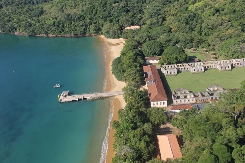 Vista aérea da Ilha Anchieta, com píer, praia e as ruínas do antigo presídio entre a mata